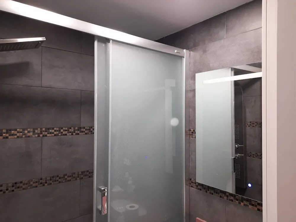 Baño con azulejo gris, cenefa de mosaico, mampara y espejo con luz