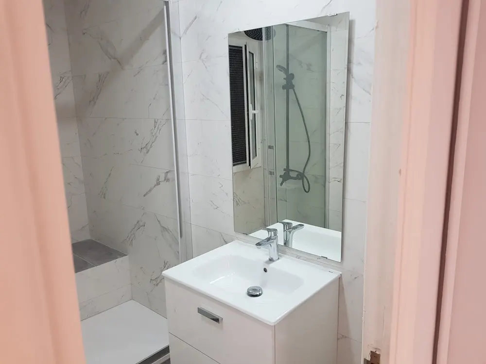 Baño con lavabo blanco, espejo y ducha con paredes de mármol claro