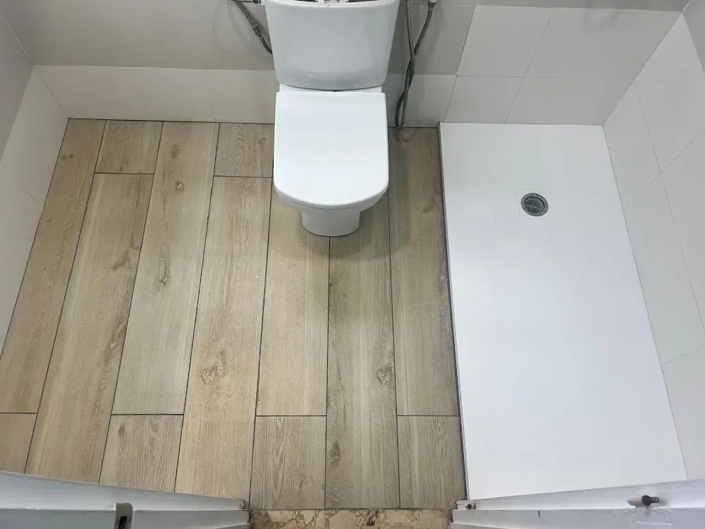 Baño con suelo de imitación madera, plato de ducha blanco e inodoro