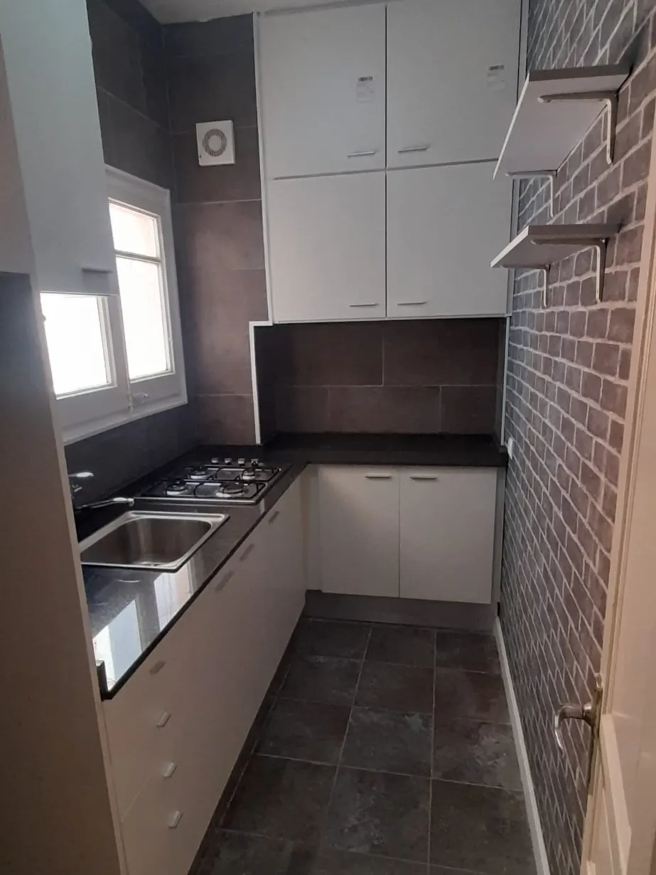 Cocina con muebles blancos, encimera oscura, fregadero y placa de gas